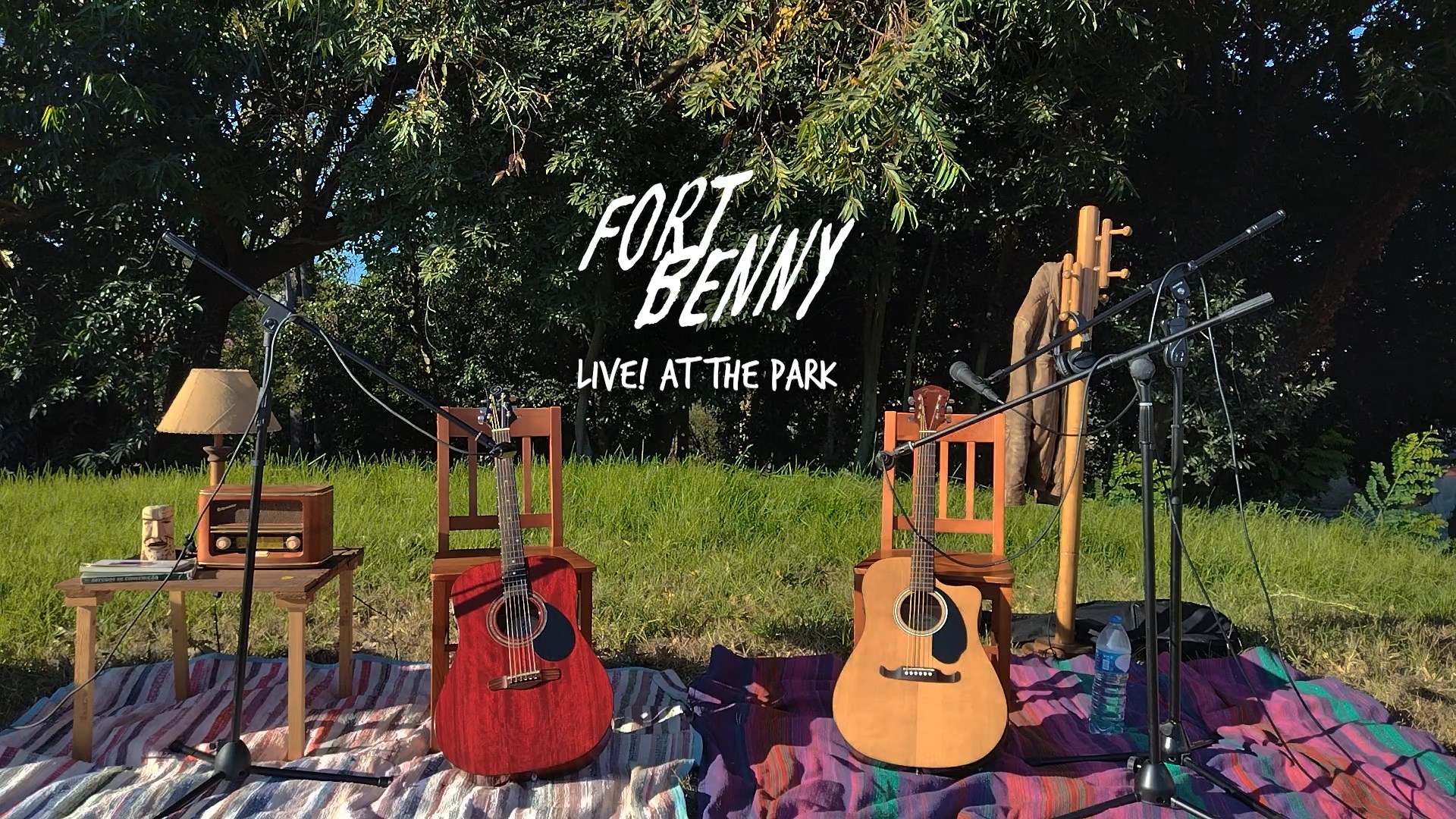 Num parque encontra-se um cenário improvisado com tapetes a fazer de chão, duas cadeiras com duas guitarras acústicas encostadas, uma mesa com um rádio, candeeiro e outros objetos. No outro lado do cenário tem um cabide com um casaco. No centro da imagem, sobre o fundo verde tem o título da imagem: Fort Benny. E, por baixo: "Live! at the Park".